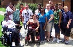 A diverse group of people, outside of a building, some with visible disabilities and some may have invisible disabilities
