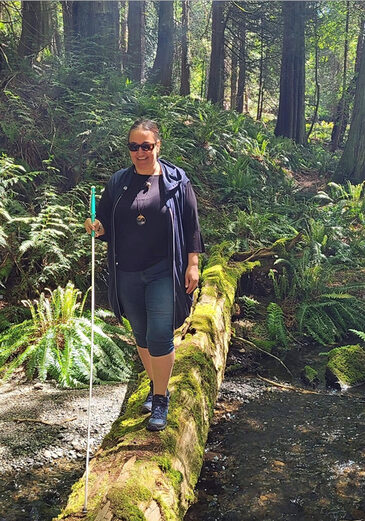 I am walking on a log over a small stream. I am using my cane along one side of the log. This helps guide me to walk straight and keep my balance. 