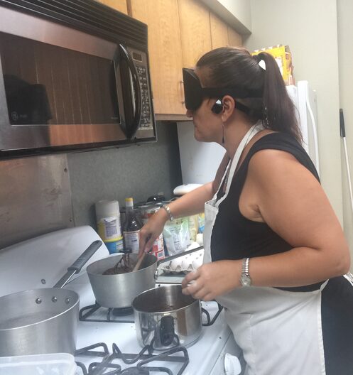 Gina standing over a gas stove that has 3 pots on it. She is cooking a meal with her trainig shades on.